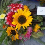 Bukiet zielny zawierający słoneczniki, różowe kwiaty, zioła i zboża. Ma przyczepioną kartkę z numerem konkursowym.