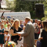 Poseł Bogusław Sonik wręcza laureatce dyplom oraz uściska jej dłoń. W tle widać tłum ludzi zgromadzony podczas wydarzenia, duży głośnik i samochód z napisem "www.wypozyczalniadekoracji.pl".