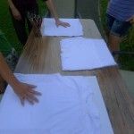 Trzy czyste białe koszulki leżą na stole. Obok nich stoi słoik z pędzlami.