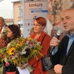 Poseł Bogusław Sonik i dwie kobiety trzymające bukiety zielne stoją na scenie. Bogusław Sonik przemawia do mikrofonu. W tle widać pionowy baner z logotypami partnerów wydarzenia.