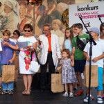 Na scenie stoi grupa dzieci oraz Liliana Sonik i mężczyzna w marynarce. Dzieci trzymają torby z nagrodami. Liliana Sonik wręcza im dyplomy.