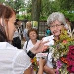 Starsza kobieta udziela wywiadu dla TVP Kraków, w ręce trzyma bukiet zielny. Za nią widać innych ludzi.