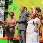 Bogusław i Liliana Sonikowie oraz prowadząca konkurs pozują do zdjęcia na tle sceny z napisem "Cudowna Moc Bukietów". Liliana Sonik trzyma bukiet zielny.