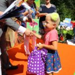 Mała dziewczynka odbiera na scenie torbę z nagrodą od posła Bogusława Sonika. Za nimi widać dwie kobiety.