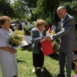 Poseł Bogusław Sonik wręcza dyplomy i nagrody dwóm starszym laureatkom, stoją na małej polanie, wokół nich widać drzewa.