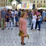 Liliana Sonik stoi na Rynku Głównym w Krakowie, trzyma mały bukiet zielny. Za nią widać kościół św. Wojciecha.