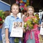 rodzeństwo Alicja i Wojciech Wójcik trzymają dyplomy wyróżnienia, dziewczynka trzyma jeszcze torbę z nagrodami a chłopiec bukiet zielny. Mają około 10 lat, w tle widać scenę i inne dzieci trzymające bukiety