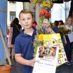 chłopiec trzyma bukiet zielny, torbę z nagrodami i dyplom wyróżnienia dla Wiktora Gałkowskiego, w tle widać scenę i inne dzieci