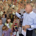 Bogusław Sonik mówi do mikrofonu w otoczeniu dzieci, trzyma dyplom i złoty puchar