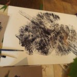 Obrazek stworzony za pomocą liści pokrytych tuszem i odbitych na kartce. Obok leżą pędzle.