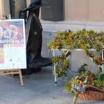 Stół zastawiony bukietami zielnymi, pod nim leży kosz wiklinowy wypełniony kwiatami, owocami i ziołami. Po lewej stronie stołu stoi tablica z napisem "Cudowna Moc Bukietów Warszawa 15 sierpnia 2013".