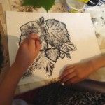 Kobieta obrysowuje na kartce wzór wykonany za pomocą odbitych w tuszu liści.