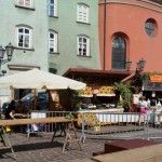 Mały Rynek w Krakowie. Ustawiono drewniane stoły, przed którymi stoją metalowe barierki. Za barierkami widać drewniane budki z parasolem.