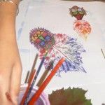 Kobieta maluje obrazek przy pomocy wzorów odbitych liści i domalowywanych do nich ilustracji.