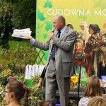 Poseł Bogusław Sonik przemawia na scenie do mikrofonu. W ręce trzyma kartki. Pod sceną zgromadziły się dzieci.
