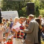 Stojący tyłem poseł Bogusław Sonik daje dyplom dziewczynce siedzącej na rękach taty. W tle widać tłum ludzi czekający na wyniki konkursu.