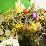 Zdjęcie bukietu zielnego zawierającego kukurydzę, zboża, żółte i fioletowe kwiaty oraz zioła.