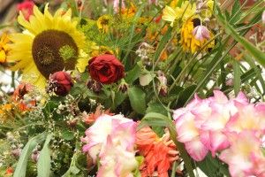Zbliżenie na bukiet zielny zawierający słonecznik, róże, mieczyk wielokwiatowy, koper włoski i inne zioła i kwiaty.