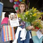 Dziewczynka Laura Kościeliska trzyma dyplom wyróżnienia i bukiet zielny w wazonie, w tle widać scenę i innych uczestników konkursu