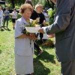 Poseł Bogusław Sonik wręcza dyplomy i nagrody starszej laureatce, stoją na małej polanie. kobieta trzyma bukiet zielny.