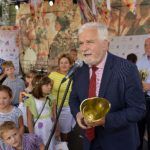 Kazimierz Barczyk mówi na scenie do mikrofonu, trzyma złoty puchar, w tle widać dzieci oraz Bogusława Sonika trzymającego puchar